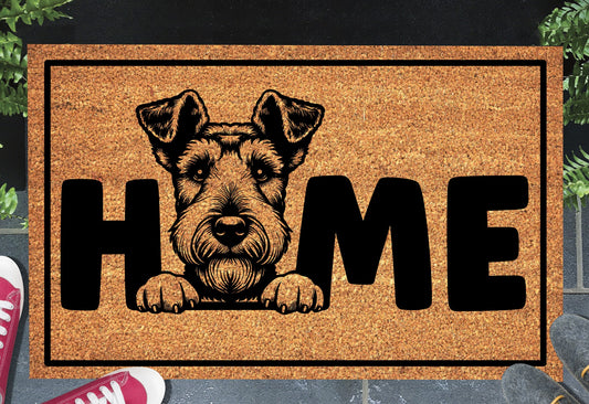 Airedale Terrier King of Terriers coir doormat with bold black HOME lettering and Airedale Terrier illustration replacing the letter O, on a natural golden coir surface with black border, styled on a slate doorstep with red sneakers and green plants