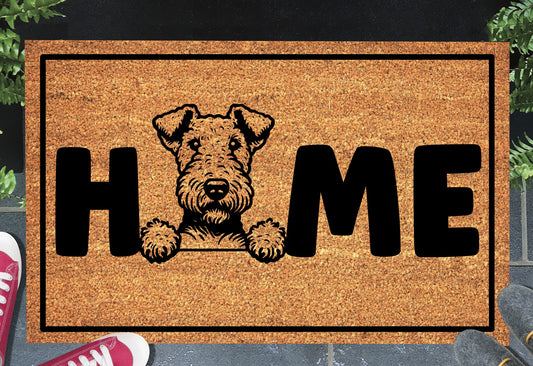 Airedale Terrier coir doormat with portrait illustration of an Airedale Terrier replacing the letter O in bold black HOME lettering, on a natural golden coir surface with black border, styled on a slate doorstep.