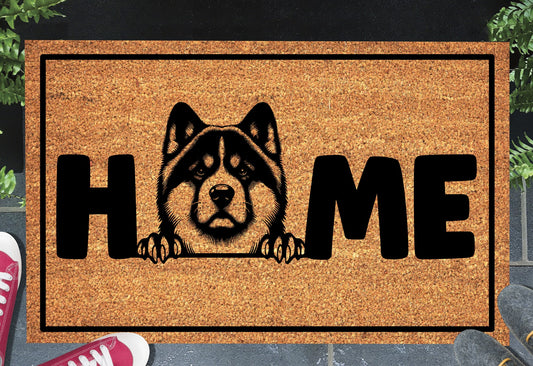 Akita coir doormat with portrait illustration of an Akita replacing the letter O in bold black HOME lettering, on a natural golden coir surface with black border, styled on a slate doorstep. 