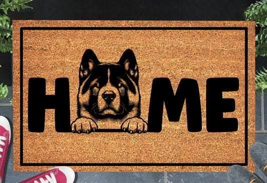 Akita coir doormat with portrait illustration of an Akita replacing the letter O in bold black HOME lettering, on a natural golden coir surface with black border, styled on a slate doorstep. 