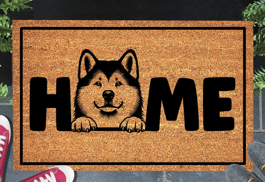 Akita coir doormat with portrait illustration of an Akita replacing the letter O in bold black HOME lettering, on a natural golden coir surface with black border, styled on a slate doorstep.