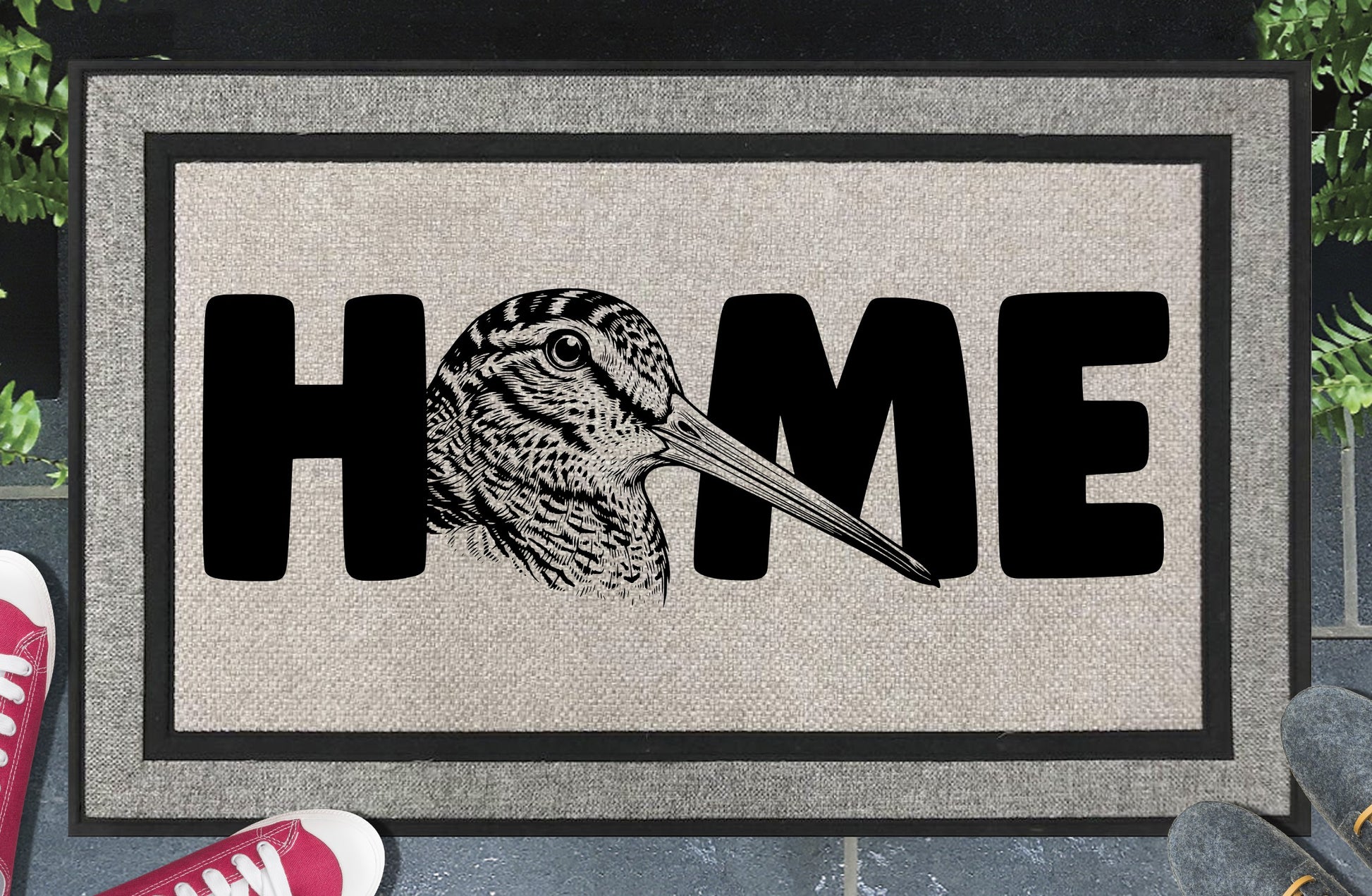 American Woodcock all-weather doormat in entryway — detailed Timberdoodle head portrait with extended bill replaces the letter O in HOME, woven polyester with linen look finish