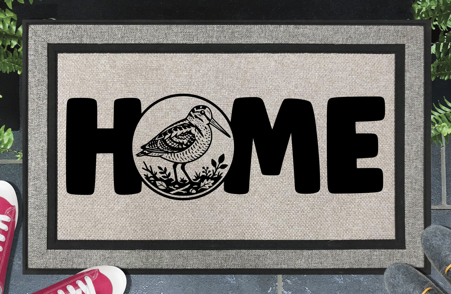 American Woodcock all-weather doormat in entryway — Bogsucker full-body illustration in circular botanical frame replaces the letter O in HOME, woven polyester with linen look finish