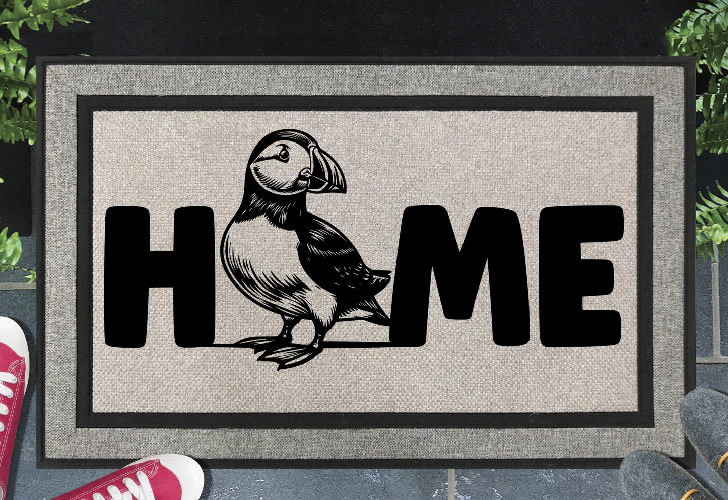 Atlantic Puffin all-weather doormat in a doorway — full-body standing Puffin illustration replacing the letter O in "HOME", UV-cured inks on woven polyester, front door entryway