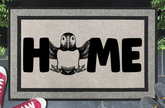 Atlantic Puffin Sea Parrot all-weather doormat in entryway — full-body standing Puffin illustration replaces the letter O in HOME on a woven polyester welcome mat