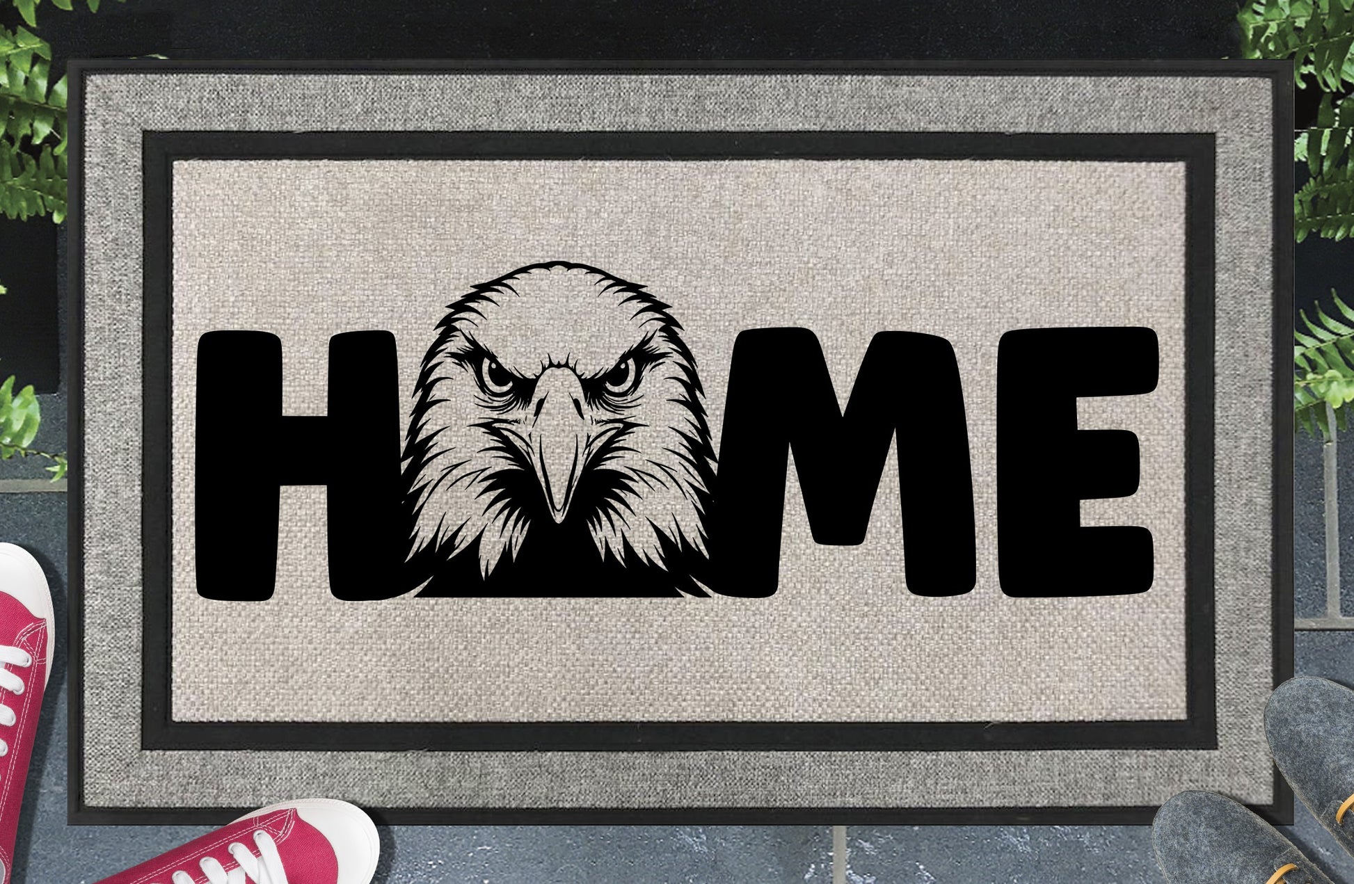 American Bald Eagle HOME all-weather doormat in doorway lifestyle shot — light grey linen-look woven polyester mat, front-facing Bald Eagle head illustration replaces the letter O in HOME, 18x30 size shown
