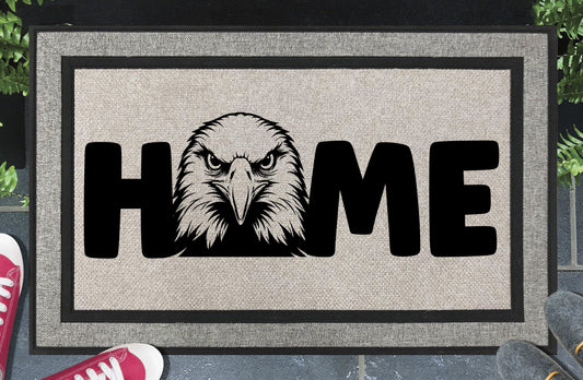 American Bald Eagle HOME all-weather doormat in doorway lifestyle shot — light grey linen-look woven polyester mat, front-facing Bald Eagle head illustration replaces the letter O in HOME, 18x30 size shown