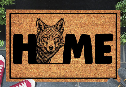 Coyote Doormat #2 shown on a front doorstep — second alternate portrait-style coyote illustration with HOME lettering on a natural coir mat with black border