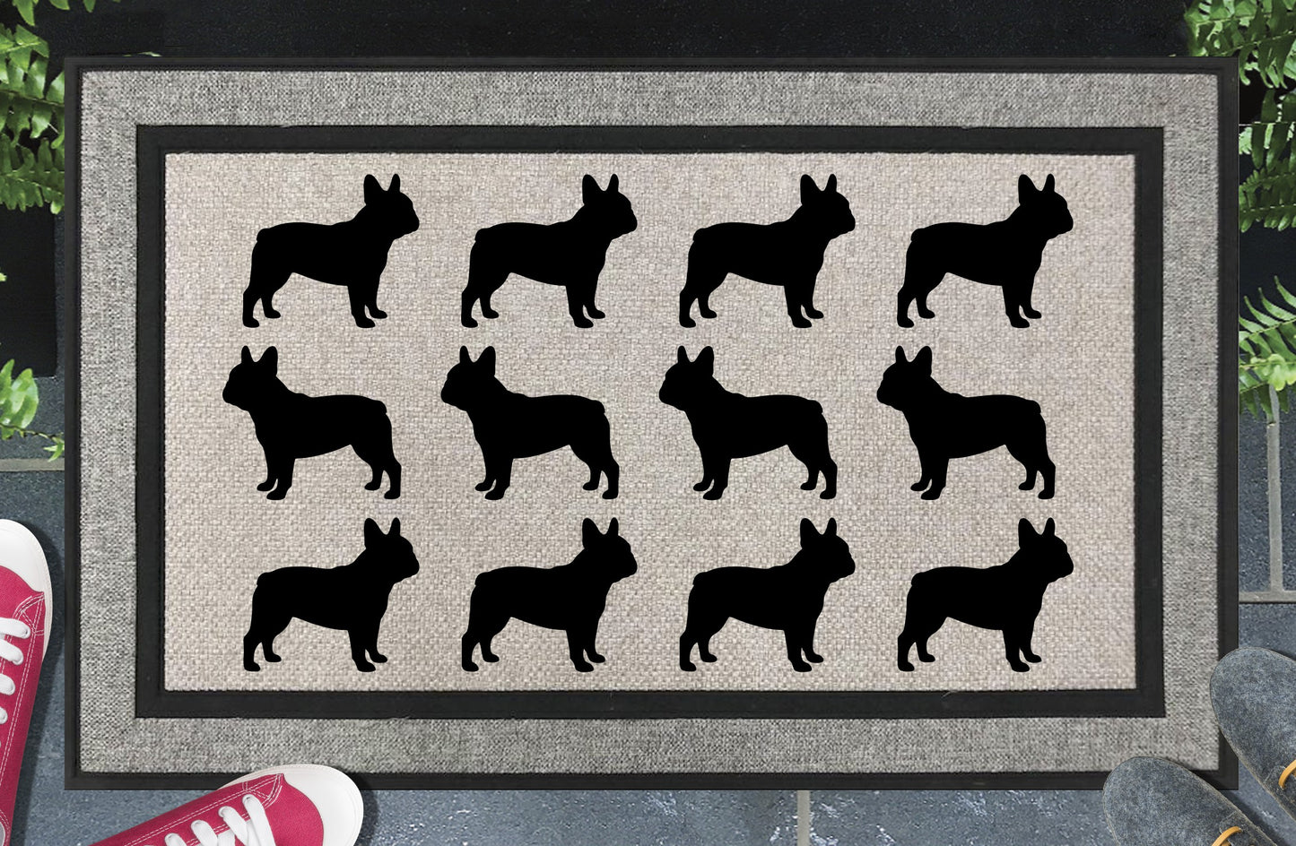 French Bulldog Parade all-weather doormat in a doorway setting — rows of French Bulldog silhouettes with bat ears, compact muscular body, and snub nose in a repeating pattern on a woven polyester mat with black border