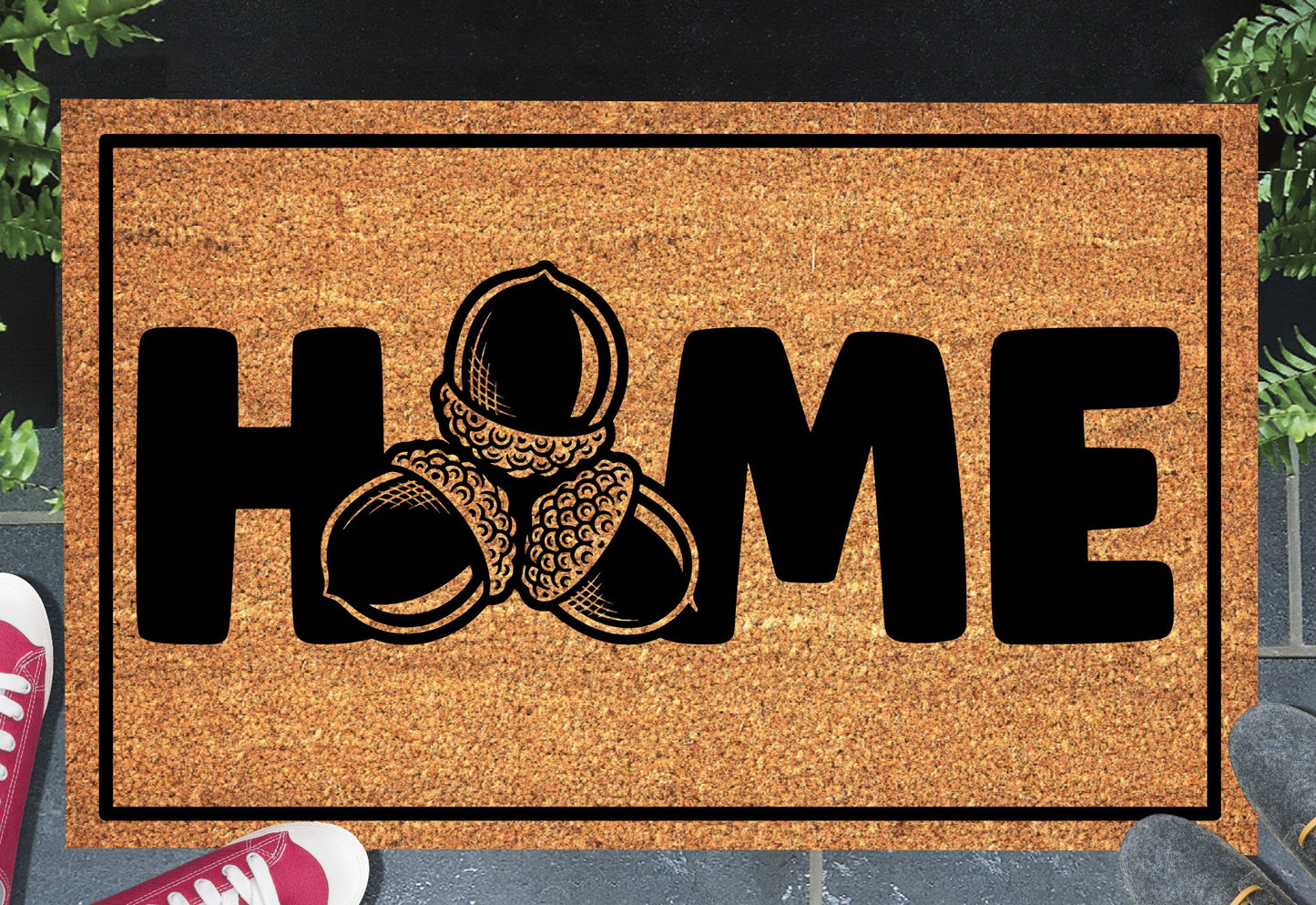 Sessile Oak Welsh Oak acorn coir doormat with bold black HOME lettering and cluster of three acorn illustrations replacing the letter O, on a natural golden coir surface with black border, styled on a slate doorstep.