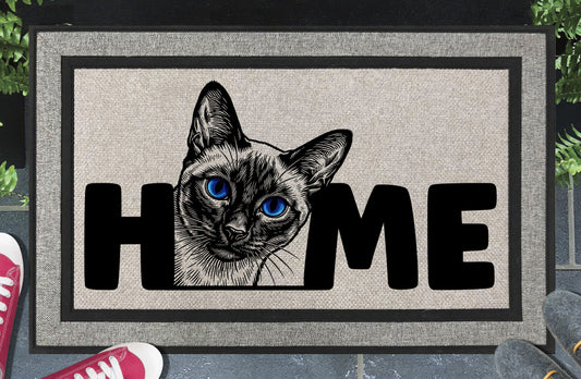 Siamese Cat all-weather doormat in a doorway setting — Meezer portrait illustration with piercing blue eyes replacing the letter O in HOME on a woven polyester mat with grey linen look finish and black border