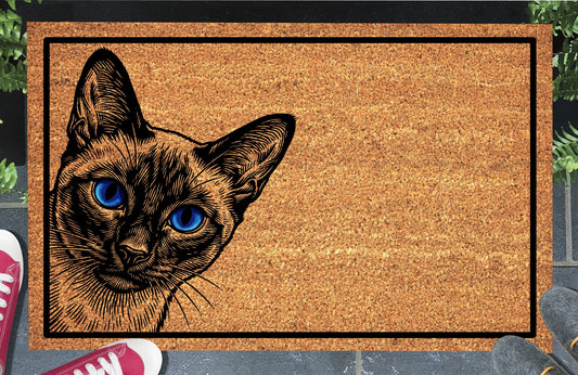 Siamese cat peeking doormat #2 in a doorway setting — Yowler peeping from the left edge with piercing blue eyes and seal point coat on a natural coir mat with black border