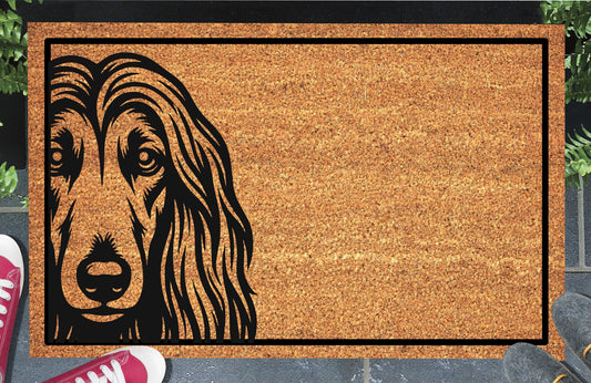 Afghan Hound Peeking Doormat #2 with bold black Affie face artwork peeking from the left edge of a bordered coir mat, shown in a doorway