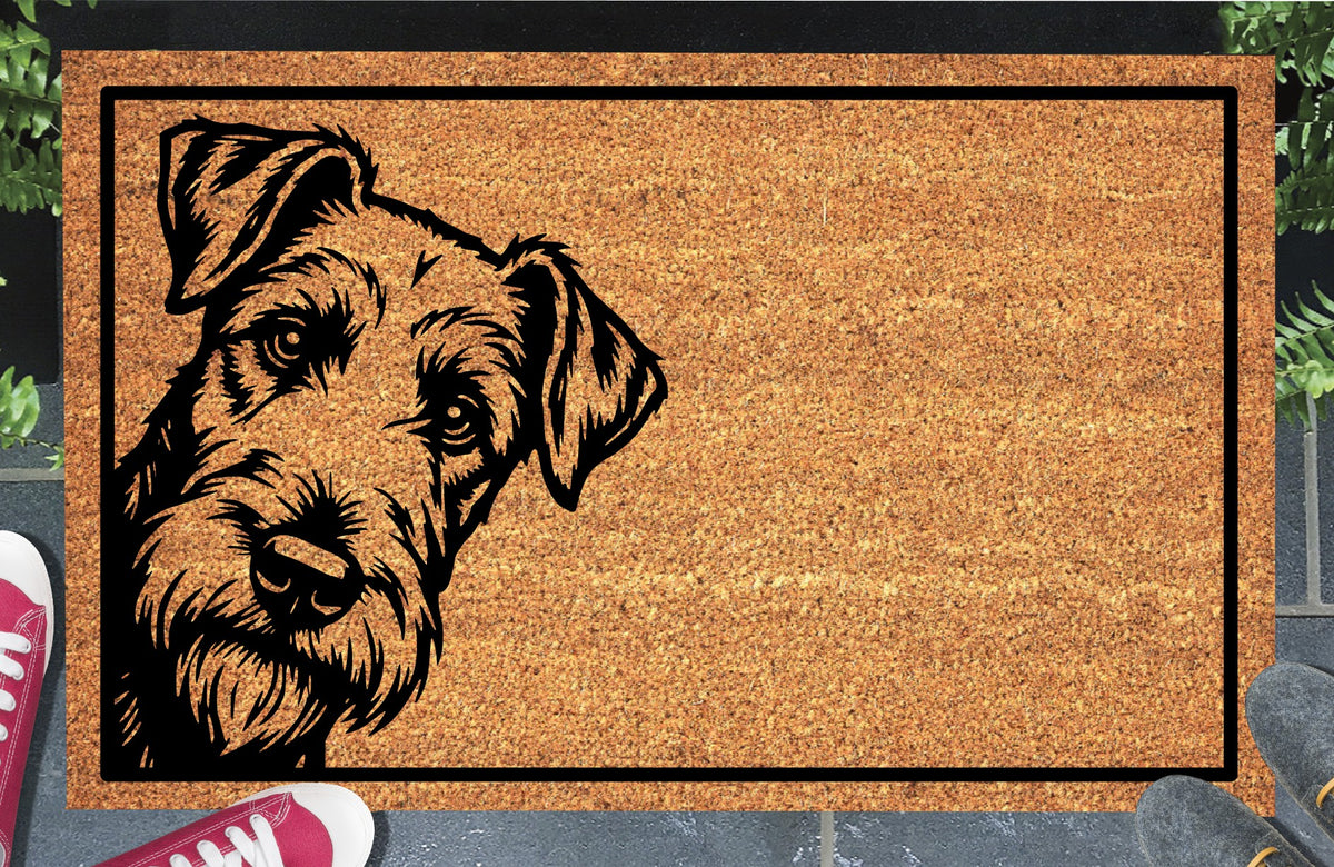 Airedale Terrier Peeking Doormat #1 with a tilted, bearded Airedale face peeking from the left edge and a black rectangular border on natural coir, shown in a doorway