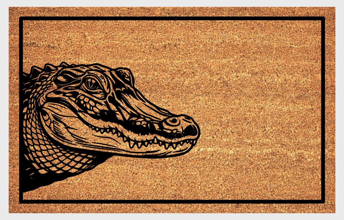Close-up of a natural coir doormat featuring a scaly Alligator peeking from the left edge with closed jaws and visible teeth.