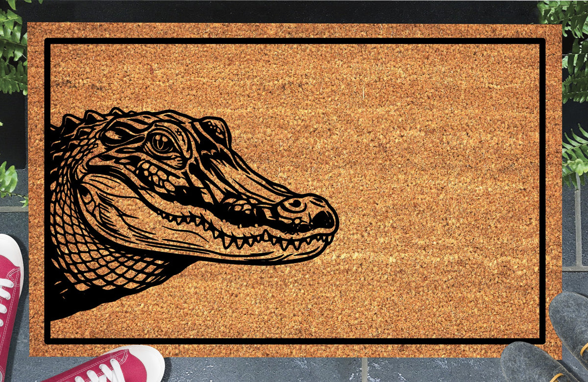Alligator peeking from the left edge of a natural coir doormat with closed jaws and a black border, shown at an entryway.