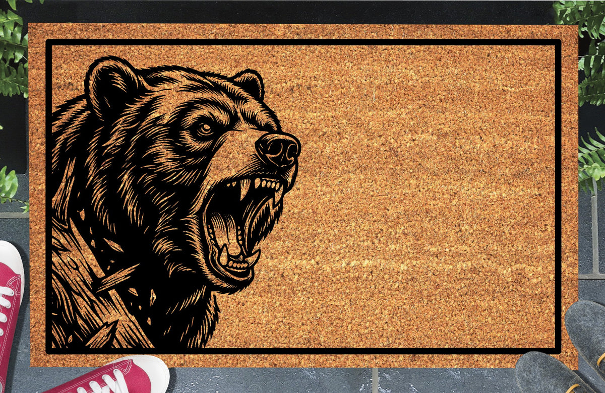 Black Bear peeking beside a tree trunk on a natural coir doormat with an open mouth and black border, shown at an entryway.