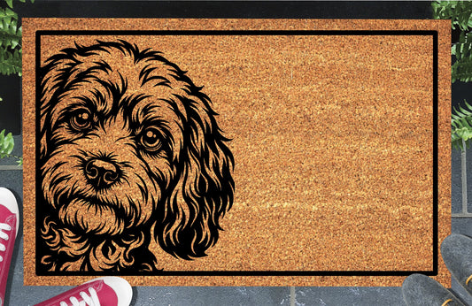 Cavapoo Peeking coir doormat #1 with a curly-coated Cavoodle portrait at the left edge and black rectangular border, shown on a doorstep