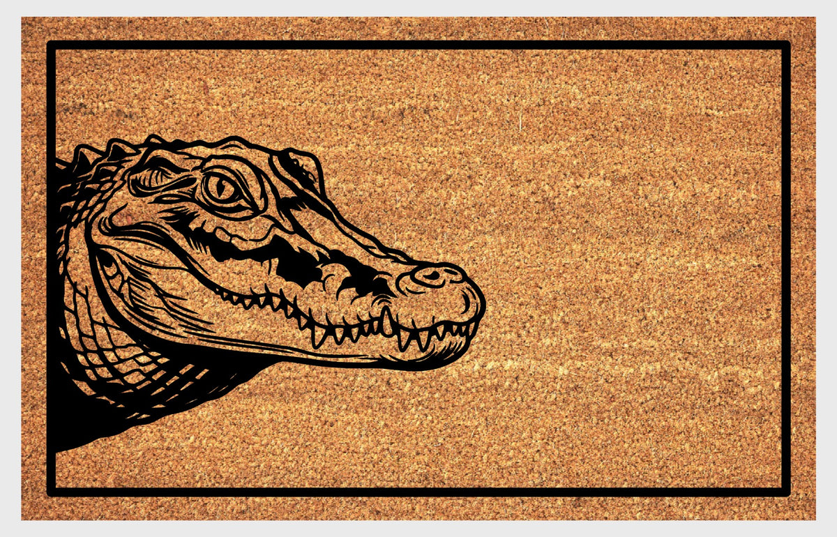 Close-up of a natural coir doormat featuring a scaly Crocodile peeking from the left edge with closed jaws and visible teeth.