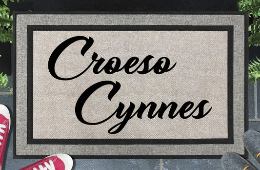 Croeso Cynnes all-weather doormat — Welsh warm welcome in bold two-line script lettering, woven polyester, linen-look finish, non-slip backing, 18x30"