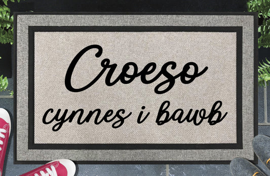 Croeso cynnes i bawb all-weather doormat — Welsh warm welcome to all in bold two-line script lettering, woven polyester, linen-look finish, non-slip backing, 18x30"