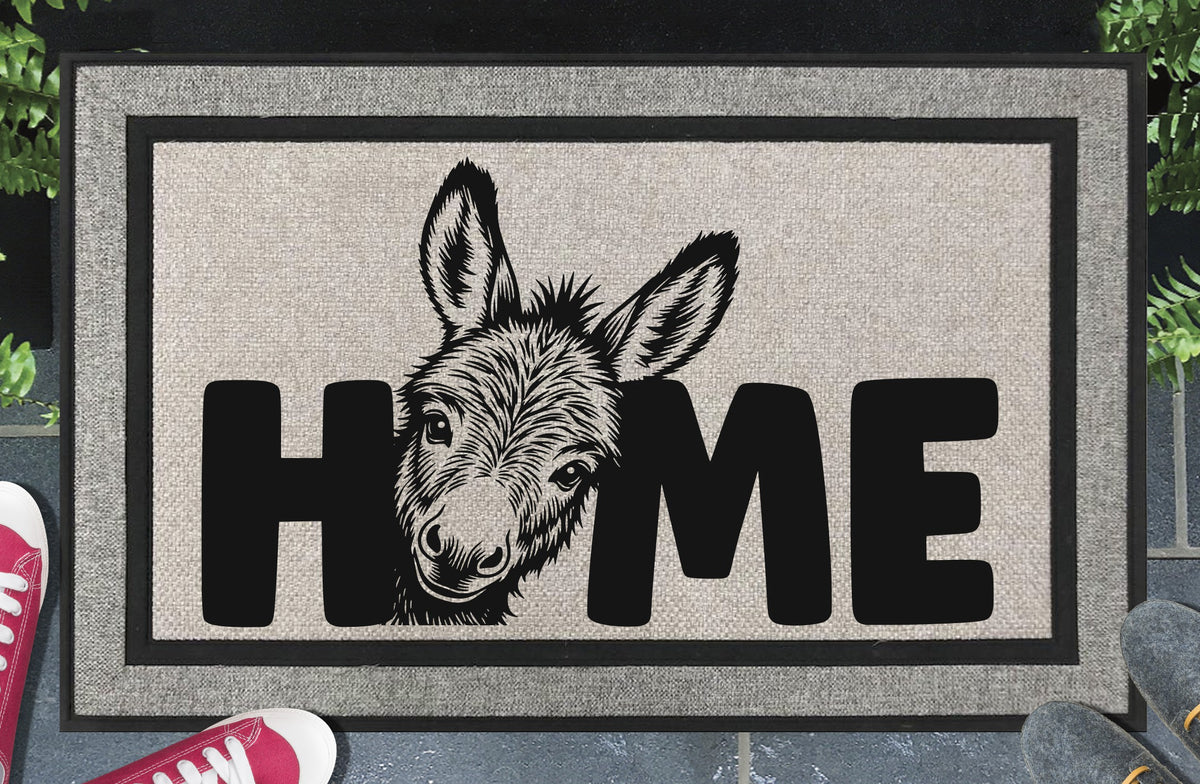 Donkey Doormat #2 All-Weather Jackass doormat — donkey face peeking up from behind the letter O in HOME, woven polyester linen-look finish, non-slip backing, flat lay on dark background