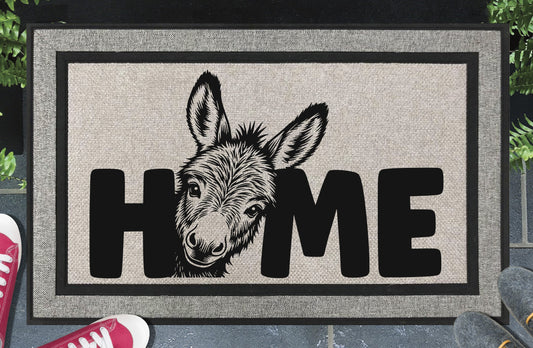 Donkey Doormat #2 All-Weather Jackass doormat — donkey face peeking up from behind the letter O in HOME, woven polyester linen-look finish, non-slip backing, flat lay on dark background