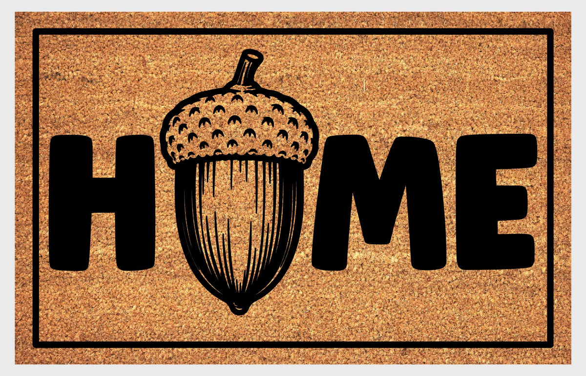 English Oak Pedunculate Oak acorn coir doormat with bold black HOME lettering and detailed acorn illustration replacing the letter O, on a natural golden coir surface with black border, plain background