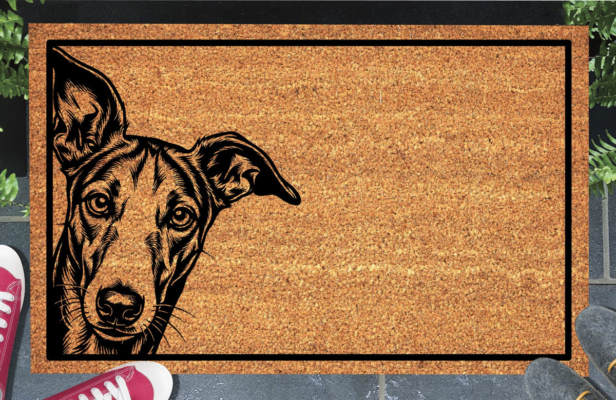 Galgo Peeking Doormat #1, Spanish Greyhound portrait peeking from the left edge inside a black border on natural coir, styled at an entryway.