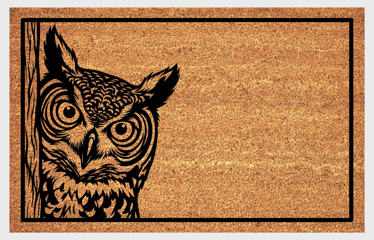 Great Horned Owl peeking coir doormat, front view showing large round eyes, feather tufts and detailed plumage within a black rectangular border.