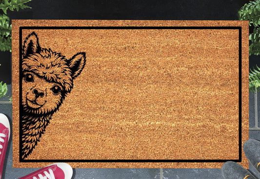 Huacaya Alpaca peeking coir doormat with a smiling Alpaca peeking from the left edge inside a black rectangular border, styled at an entryway.