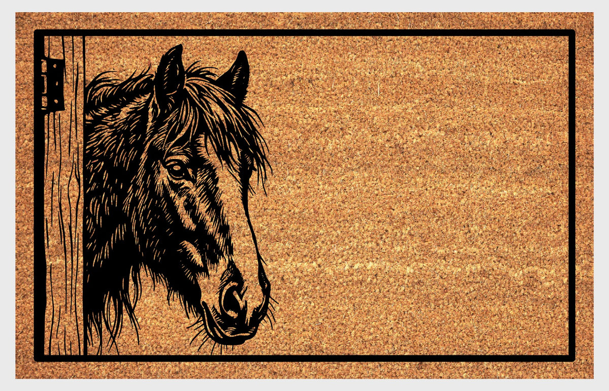 Close-up of an Irish Cob Horse peeking natural coir doormat, showing its tousled mane, broad facial blaze and the wooden stable door and hinge.