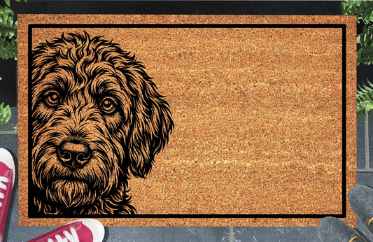 Labradoodle Peeking Doormat #1, shaggy Doodle portrait on the left with a black border, natural coir mat styled at an entryway.