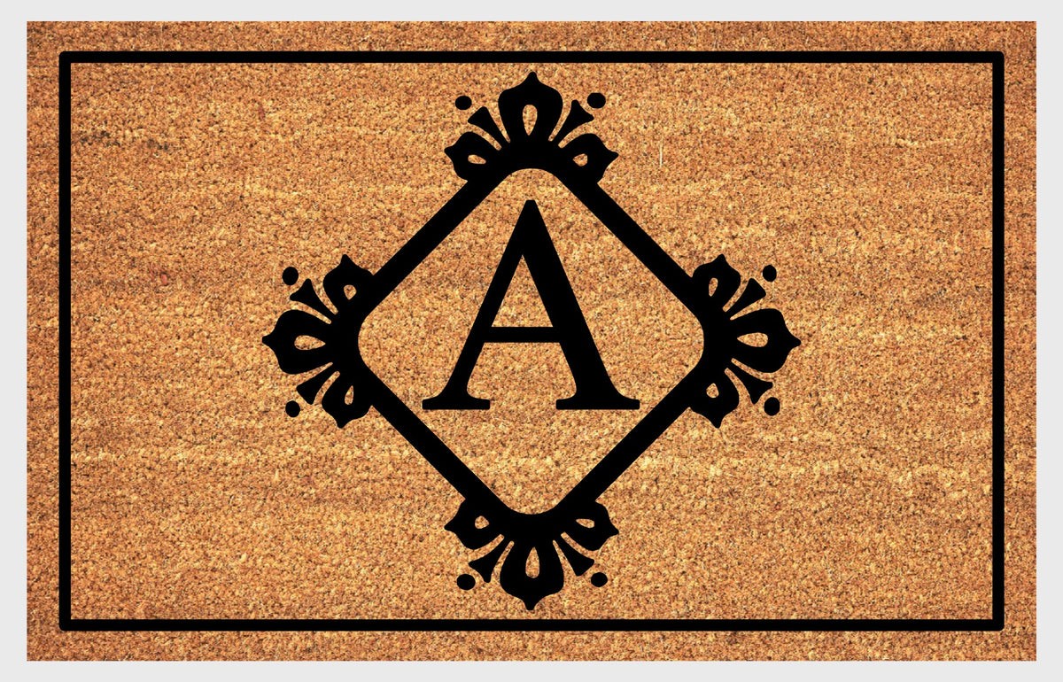 Monogram Letter A doormat in natural coir with an ornate serif letter A in a diamond frame with fleur-de-lis style flourishes and dot accents, with a black border, shown flat.
