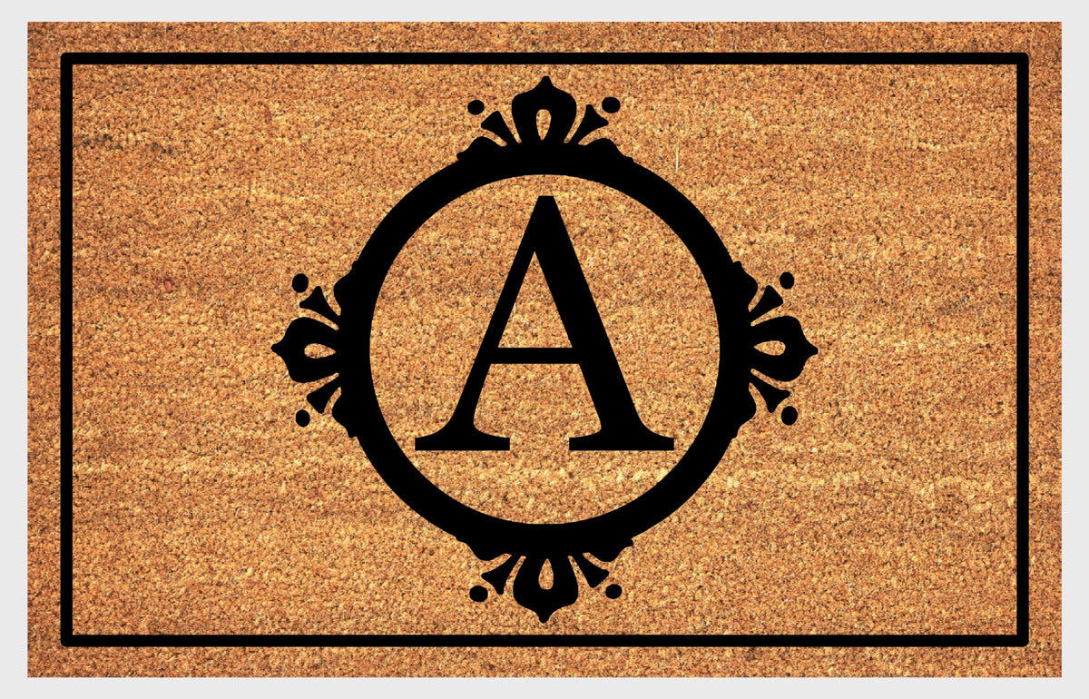 Monogram Letter A doormat in natural coir, featuring a serif A in a circular frame with fleur-de-lis style flourishes, dot accents and a black rectangular border, shown flat.