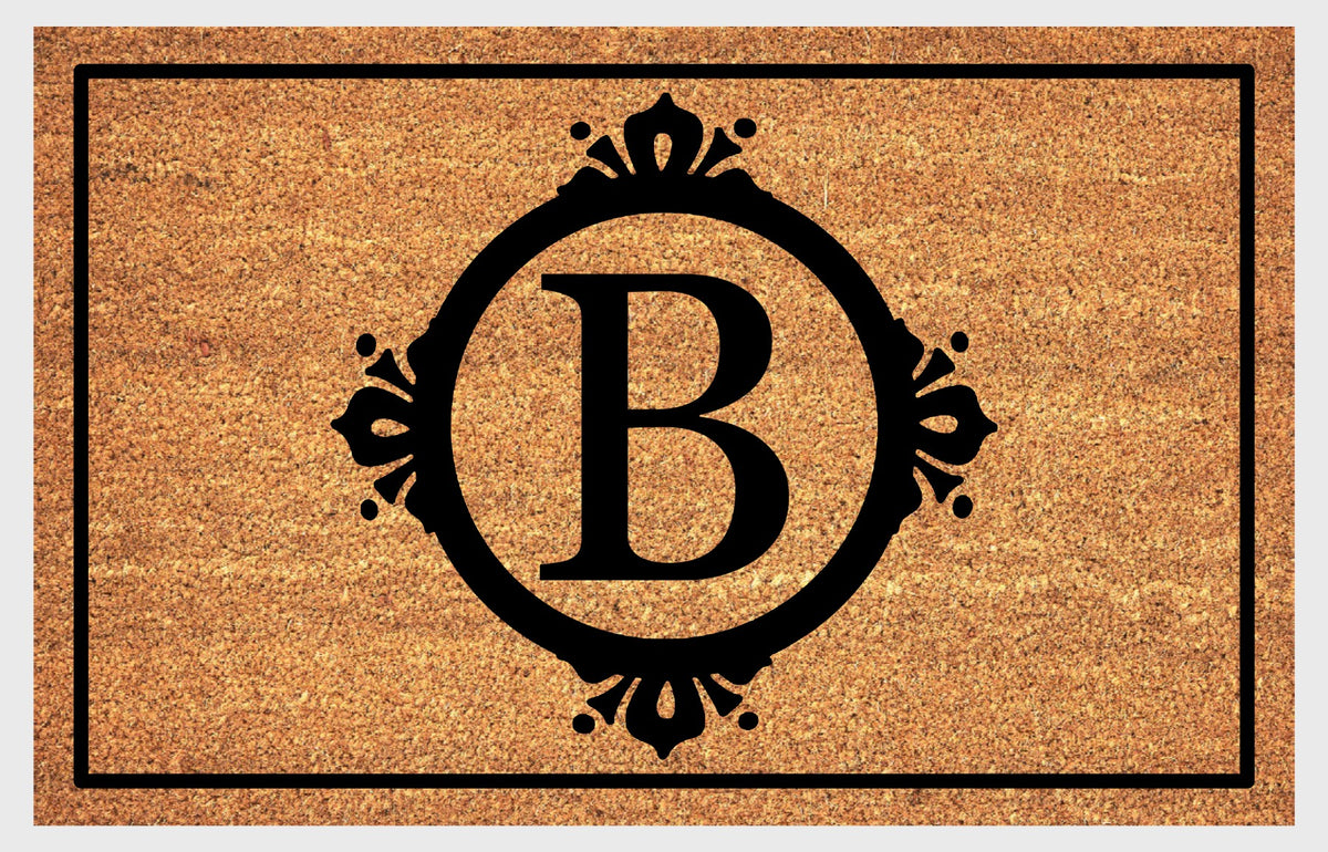 Monogram Letter B doormat in natural coir, featuring a serif B in a circular frame with fleur-de-lis style flourishes, dot accents and a black rectangular border, shown flat.