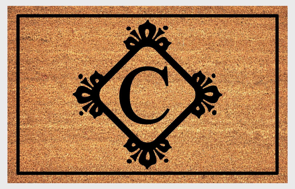 Monogram Letter C doormat in natural coir with an ornate serif letter C in a diamond frame with fleur-de-lis style flourishes and dot accents, with a black border, shown flat.