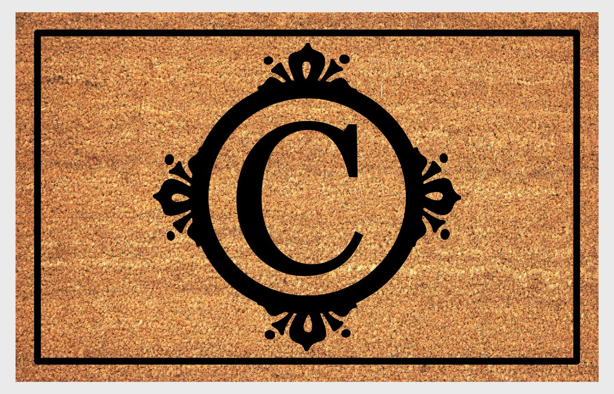 Monogram Letter C doormat in natural coir, featuring a serif C in a circular frame with fleur-de-lis style flourishes, dot accents and a black rectangular border, shown flat.