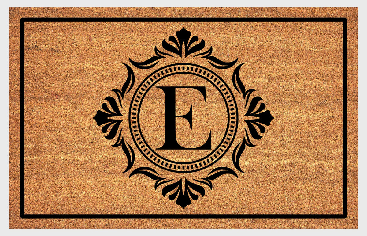 Monogram Letter E doormat in natural coir with an ornate serif letter E in a dotted circular frame, fleur-de-lis style flourishes, and a black border, shown flat.