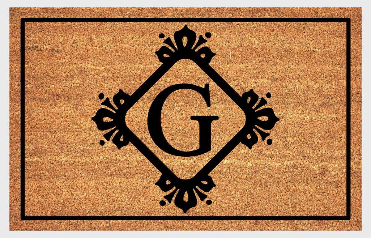 Monogram Letter G doormat in natural coir, featuring a serif G in a diamond frame with fleur-de-lis style flourishes, dot accents and a black border, shown flat.