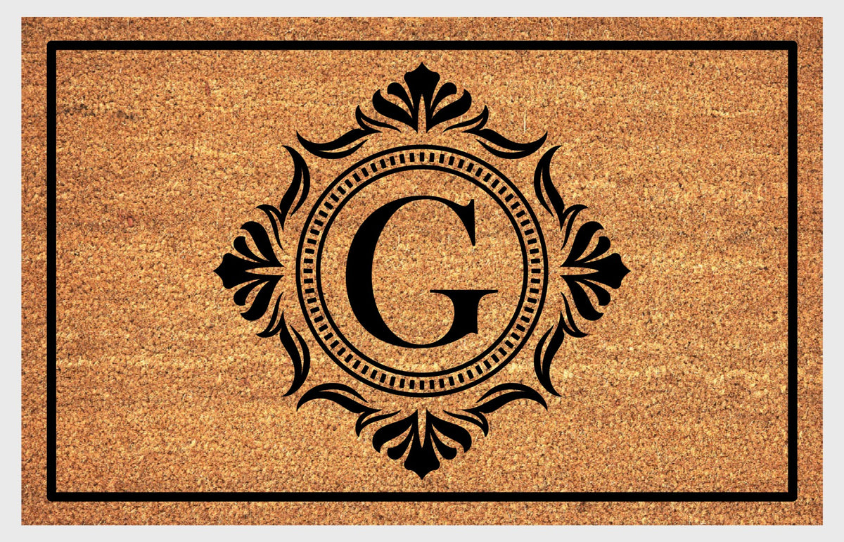 Monogram Letter G doormat in natural coir with an ornate serif letter G in a dotted circular frame, fleur-de-lis style flourishes, and a black border, shown flat.