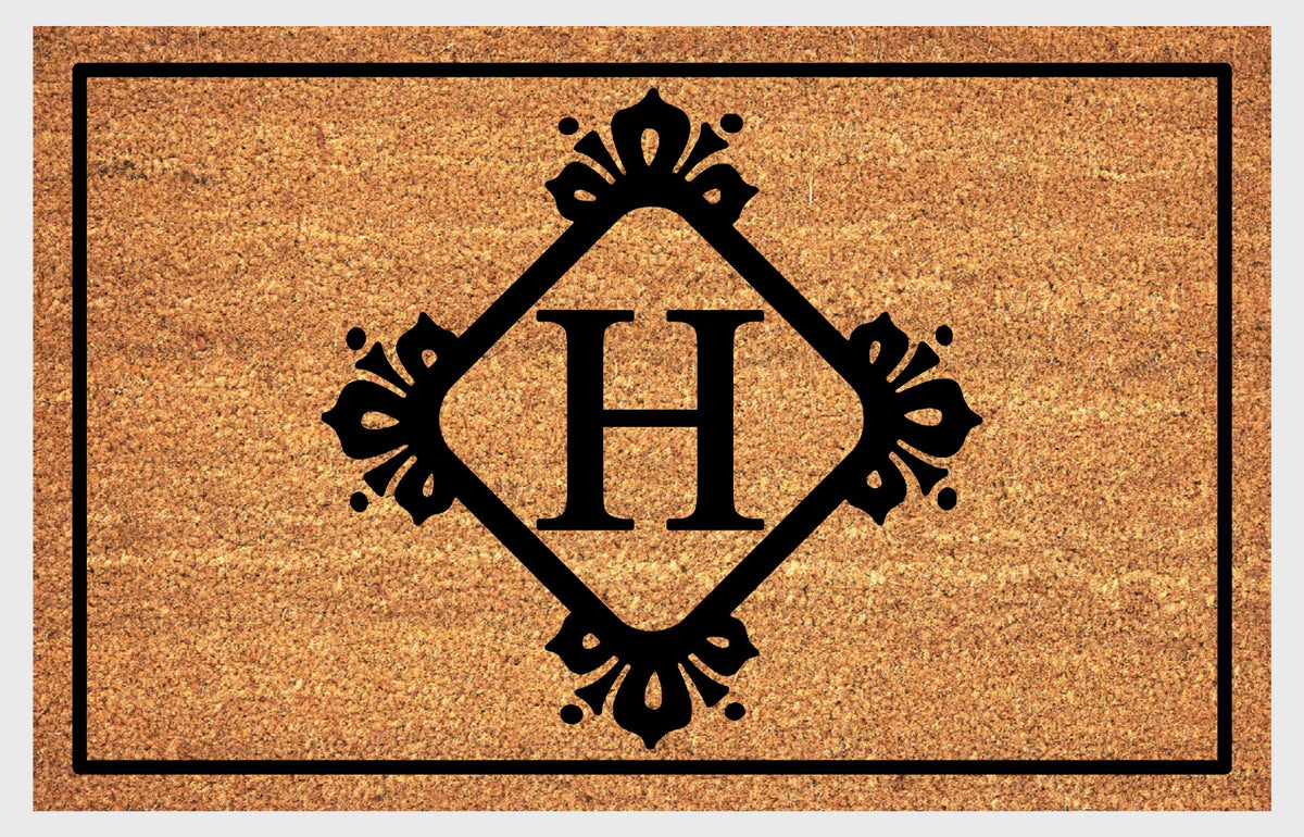 Monogram Letter H doormat in natural coir, featuring a serif H in a diamond frame with fleur-de-lis style flourishes, dot accents and a black border, shown flat.