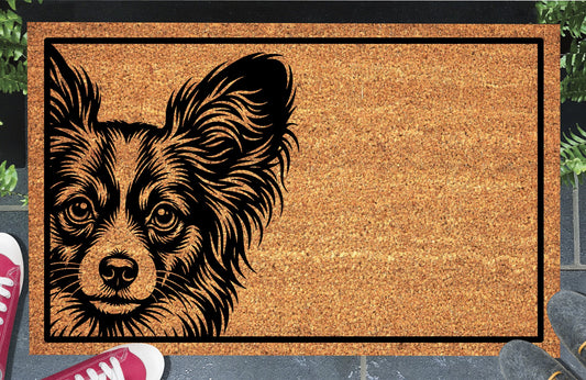 Papillon doormat with large fringed ears and expressive eyes inside a black border, displayed on a paved doorstep.