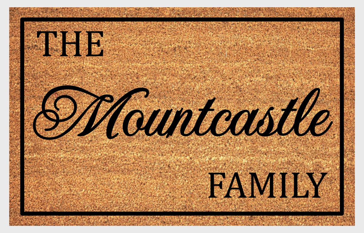 Script-style family name doormat showing “THE” above flowing script and “FAMILY” below, framed by a black rectangular border.