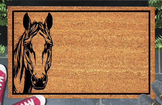 Quarter Horse peeking doormat in natural coir, featuring a black horse portrait peeking from the left edge with upright ears, expressive eyes and a swept forelock and mane inside a black rectangular border, displayed on a doorstep.