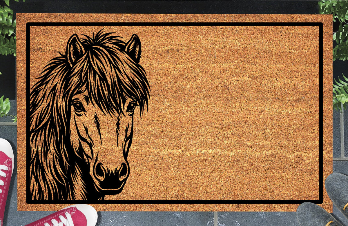 Shetland Pony peeking doormat in natural coir, featuring a black pony portrait peeking from the left edge with small upright ears, expressive eyes, a heavy forelock and a shaggy mane inside a black rectangular border, displayed on a doorstep.