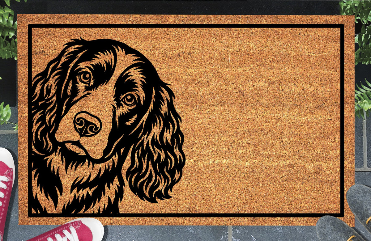 Springer Spaniel doormat with a tilted head, expressive eyes and long wavy ears inside a black border, displayed on a paved doorstep.