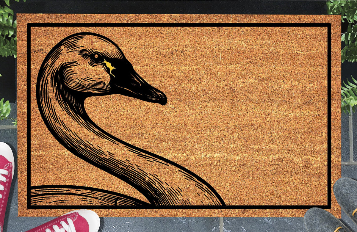 Tundra Swan peeking from the left edge of a natural coir doormat, with a sweeping curved neck, black bill and small yellow patch near the eye, within a black border at a doorstep.