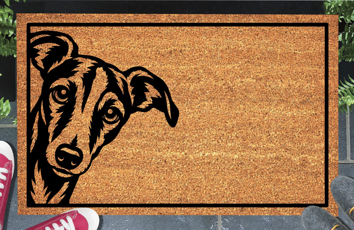 Whippet Doormat #2, natural coir mat with a tilted-head Whippet peeking from the left edge inside a black border, styled at an entryway.