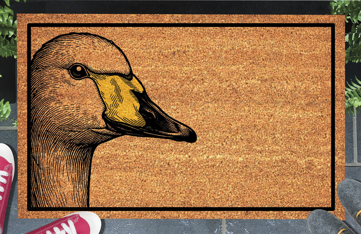 Whooper Swan peeking from the left edge of a natural coir doormat, with a detailed head and neck, yellow-and-black bill and black rectangular border, shown at a doorstep.